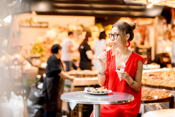 Young woman in red dress eating jamon traditional spanish dry-cured ham sitting at the Barcelona food market