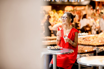 Young woman in red dress eating jamon traditional spanish dry-cured ham sitting at the Barcelona food market