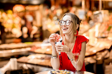 Young woman in red dress eating jamon traditional spanish dry-cured ham sitting at the Barcelona food market