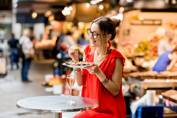 Young woman in red dress having lunch with mussels and rose wine sitting at the food market