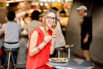 Young woman in red dress having lunch with mussels and rose wine sitting at the food market