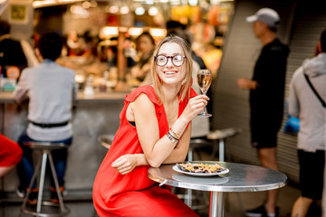 Young woman in red dress having lunch with mussels and rose wine sitting at the food market