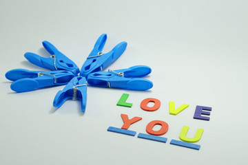 Blue cloth pin arrangement for flower concept with multicolor wood letter LOVE YOU word on white background