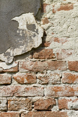 Wall of old, red baked brick with fallen plaster and layer of gray paint; Architectural background, texture, pattern; Copy space.