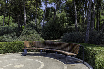Half round curved crescent shaped bench in the park with trees and bushes in background