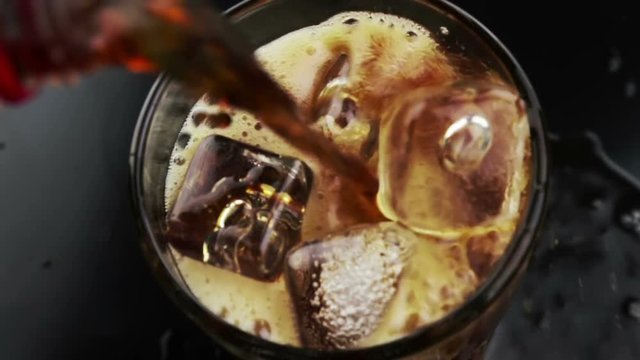 top of view pouring of fresh coke in the drink glass with ice cubes on black background, fun and summer time concept