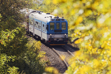 Transportation. Passenger train runs along tracks between trees in autumnal landscape