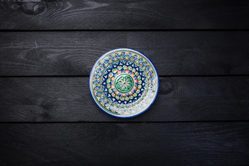Oriental ceramic plate with beautiful colorful ornament. Top view dark wooden background
