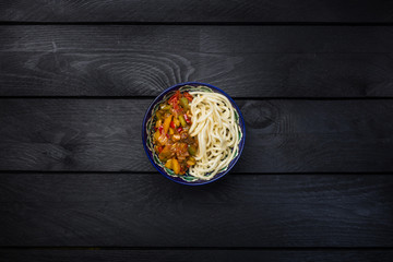 Traditional asian noodle lagman with vegetables and meat. Top view dark wooden background