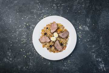 Pilaf on plate with oriental ornament on a dark background. Central-Asian cuisine - Plov. Top view