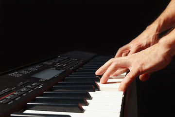 Hands of musician playing the electronic organ on a black background