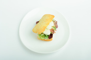 Sandwich with mozzarella, tuna, tomato and salad leaves on a plate isolated on white background