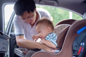 asian father helps his cute little asian 1 year old toddler baby boy child to fasten belt on car seat