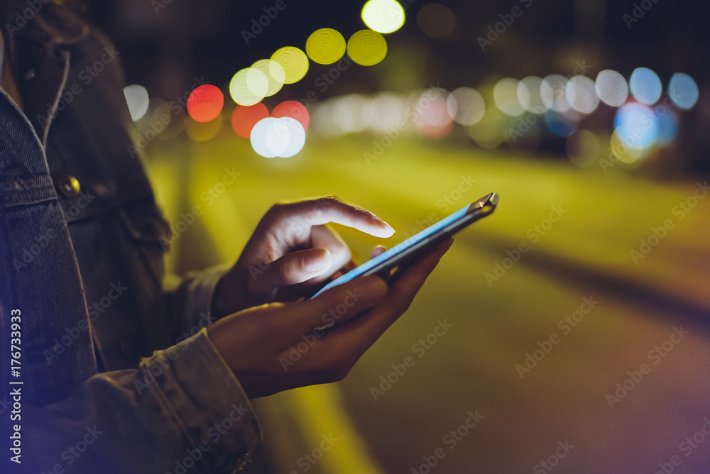 Wall mural girl pointing finger on screen smartphone on background illumination glow bokeh light in night atmos