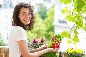 Young woman taking care of her plants and vegetables on her city balcony garden - Environment and...