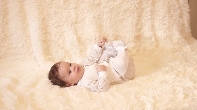 Infant lying on his back, moves his feet on white blanket.