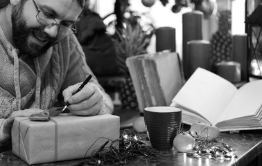monochrome beard man writing christmas gifts on a table