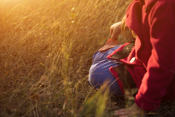 Cropped shot of little girl sitting on grass holding leaf relaxing on sunset at the autumn day