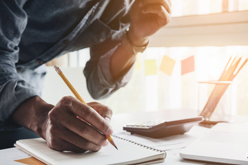 Close up accountant man using calculator while writing make note about cost profit at home office.