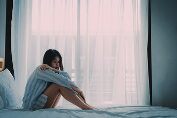 A beautiful Asian woman sitting on a bed looking sad and lonely