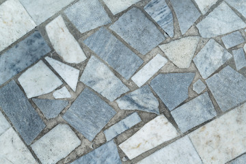 Marble tiles of different shapes laid out on a flat surface. The tiles are rectangular and triangular in shape. Have gray, beige and blue. The seams between the tiles filled with concrete or cement.