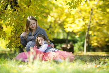 Fototapeta premium Pregnant mother with her daughter lies in the autumn park