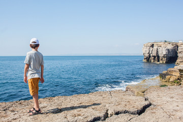 The boy is standing on the rocks