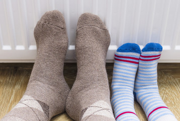  man and a child in winter socks warm their feet near the heater.