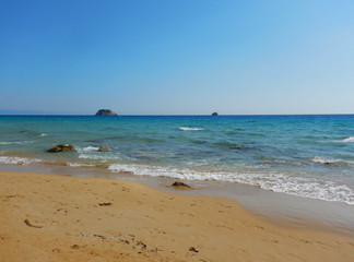 Fototapeta na wymiar An empty sandy golden beach with turquoise sea near a big stone cliff in Cephalonia or Kefalonia in Greece.