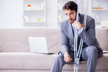 Businessman with crutches and broken leg at home working