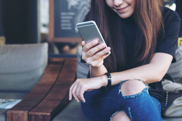 Closeup image of a beautiful Asian woman holding and using at smart phone sitting cross leg in...