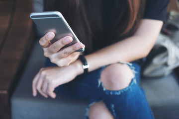Closeup image of a woman's hand holding and using at smart phone sitting cross leg in modern cafe