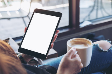 Mockup image of woman's hands holding black tablet pc with white blank screen and coffee cup of hot latte sitting in modern cafe