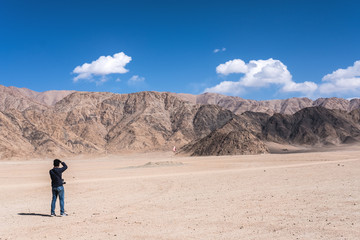 Fototapeta na wymiar A man photographer taking a landscape photo of mountains and blue sky in Ladakh , India