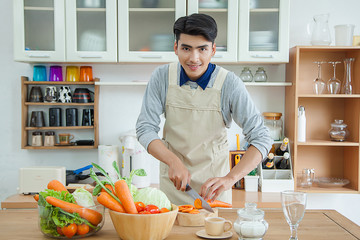 Asian young man is cooking,Portrait of young man looking recipe on laptop while cutting broccoli on board in the kitchen