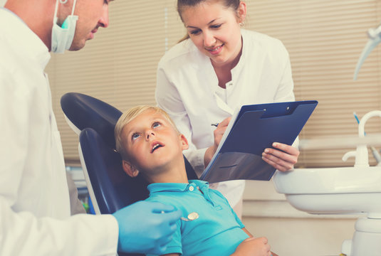Dentist guy with assistant are diagnosticating to young patient which is sitting