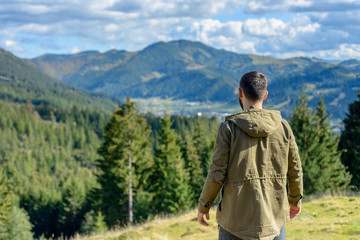 Beautiful young guy is a traveler on the top of the mountain, enjoying a panoramic view of the town in the mountains.
