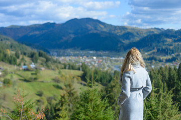 Naklejka na ściany i meble Beautiful young girl standing on the top of the mountain, and enjoying the panorama of the city in the mountains. 