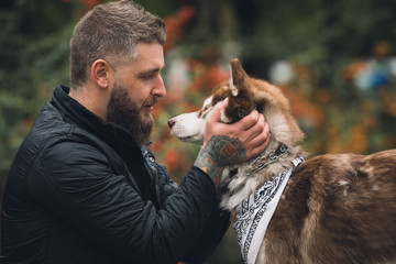 Portrait of man with a dog husky looks at each other in park at the autumn day © antgor