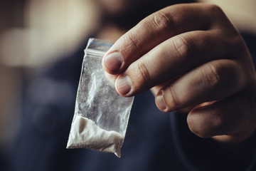 Man hand holds plastic packet or bag with cocaine or another drugs, drug abuse and danger addiction concept - obrazy, fototapety, plakaty