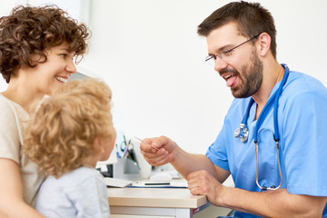 Obraz premium Portrait of friendly pediatrician examining little child sitting on mothers arms during appointment in office