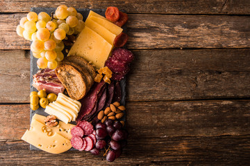 Cheese and meat appetizer selection. Prosciutto di Parma, salami, bread sticks, baguette slices, olives, grapes and nuts on rustic wooden background.