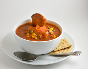 Hot Fresh Garden Vegetable Soup in white bowl with spoon and whole wheat saltine crackers.