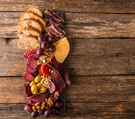 Cheese and meat appetizer selection. Prosciutto di Parma, salami, bread sticks, baguette slices, olives, grapes and nuts on rustic wooden background.