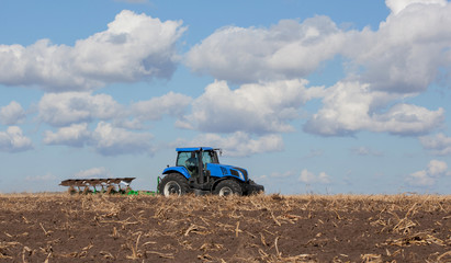 Naklejka premium a large blue tractor, plowing field against the beautiful sky. Work of agricultural machinery. Harvest