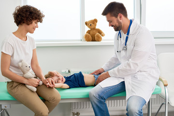 Portrait of smiling doctor examining stomach of little boy palpating in to see where it hurts