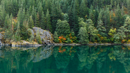 Green colored lake water with reflection of evergreen trees, autumn colors and rocks along the shoreline.