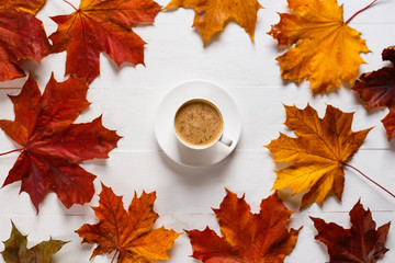 The concept of autumn, bright colors and cheerfulness. A mug of coffee with milk on a white wooden table in a composition with autumn maple leaves.