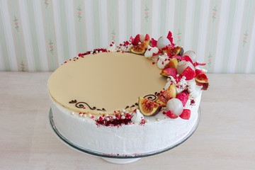 White cake with white chocolate on the wall interior background. Cake decorated with fruits lychees and figs. With blank, place for text.