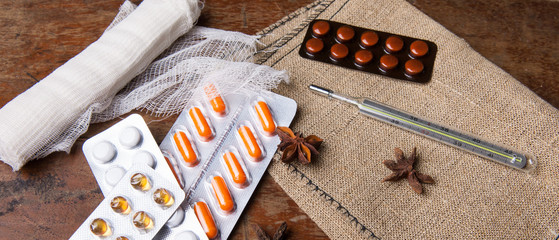 Medical bandage, pills and thermometer on the wooden background. Close up.